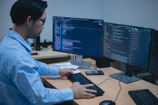 Computer programmer analyzes code across multiple screens while developing and testing software, representing coding, problem solving, productivity, and modern IT work.