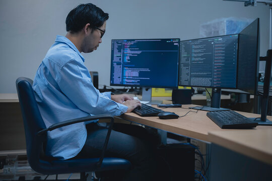 Computer programmer analyzes code across multiple screens while developing and testing software, representing coding, problem solving, productivity, and modern IT work.