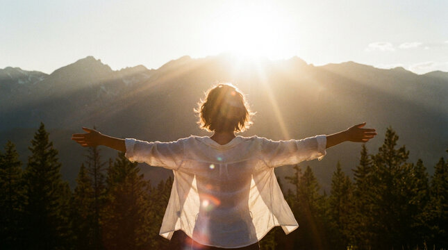 Woman with arms outstretched enjoying the sunrise over mountain peaks
