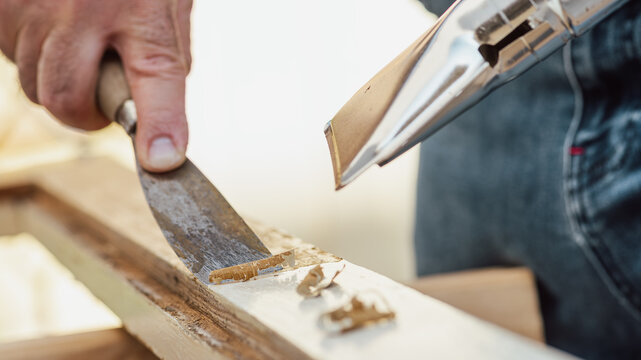 Carpenter using heat gun and wood scraper removes paint from old wooden window. Construction industry, carpentry. Restoration. 