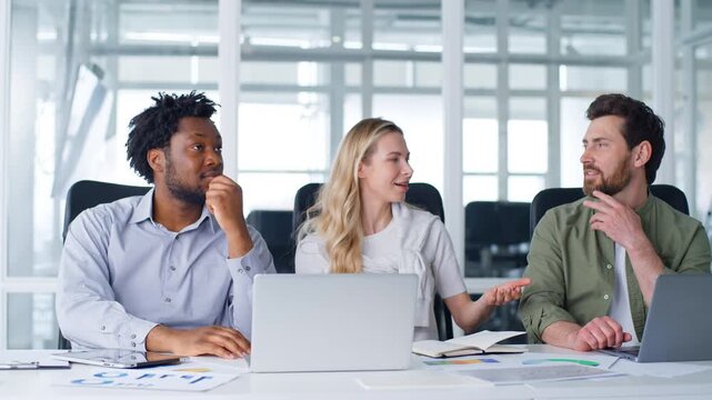 Pensive multiethnic business team working talking in office coworking with laptops Caucasian woman explaining drawing in air with pen to diversity men three agents brainstorming talk pensive work