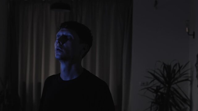 Confused man standing alone and looking upward in emotional shock and numbness, struggling to process a difficult life situation, slow camera pull-out in a dark cinematic evening interior