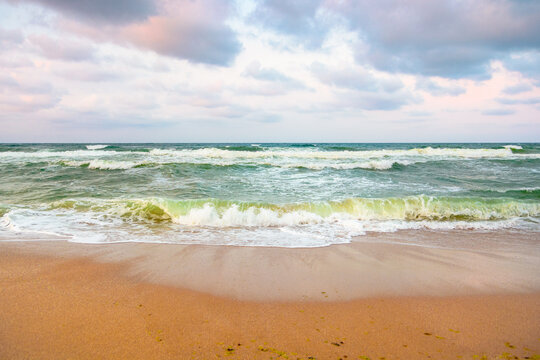 golden cloudy evening above the green sea waters. waves crashing the sandy beach. clear horizon. changing windy weather. dramatic sky