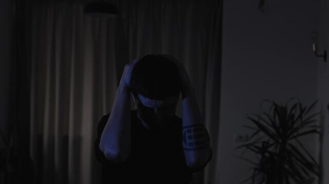 Overwhelmed man holding his head and suddenly shouting in emotional distress, expressing frustration and inner turmoil during a difficult life situation in a dark cinematic evening interior