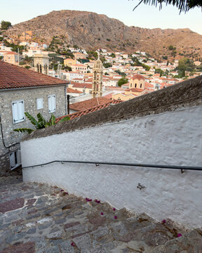 Cobbled stairway descends past whitewashed walls toward church towers in Hydra, Greece
