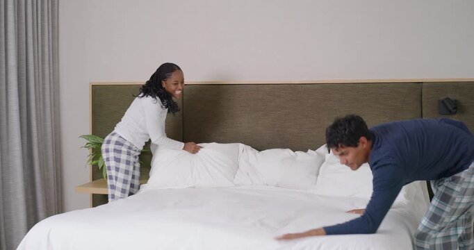 African American couple entering bedroom making bed in PJs fluffing pillows hugging walking apart