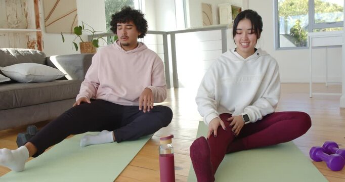Couple conversing and adjusting mats and dumbbells, performing seated hamstring stretches