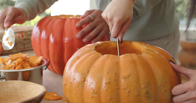 After removing tops, couple scraping pumpkin with knife, ladling pulp at table by window to carve