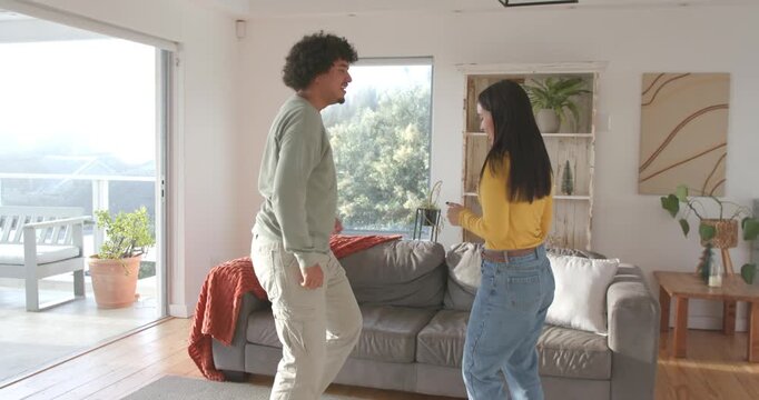 Couple dancing after sharing smiles in living room in front of gray sofa, man mirroring