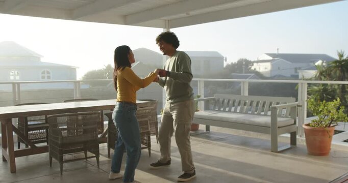 Couple grasping hands, practicing short partner dance on covered porch near wooden table