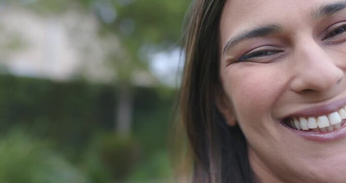 Adult woman shifting slightly toward camera, smiling and broadening laugh in garden with hedges