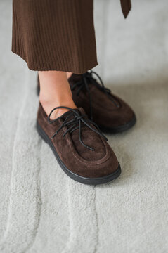 Brown suede shoes with lace-up detail worn over corduroy hem on light gray carpet (close-up) with indoor mood and texture-rich look and everyday style that highlights footwear and fabric contrasts.