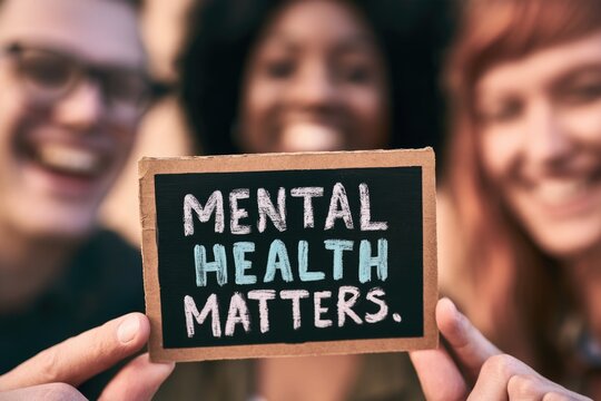 Three smiling people hold a small chalkboard sign that reads "MENTAL HEALTH MATTERS.