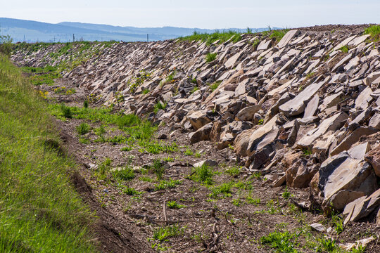 Stone-lined drainage channel for flood protection and erosion control in a rural agricultural landscape with green fields, hills, and utility infrastructure.