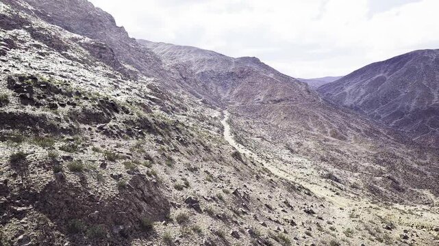 Drone survey arid hillside route revealing erosion patterns and scrub vegetation, high vantage useful for conservation mapping, geology study and rural