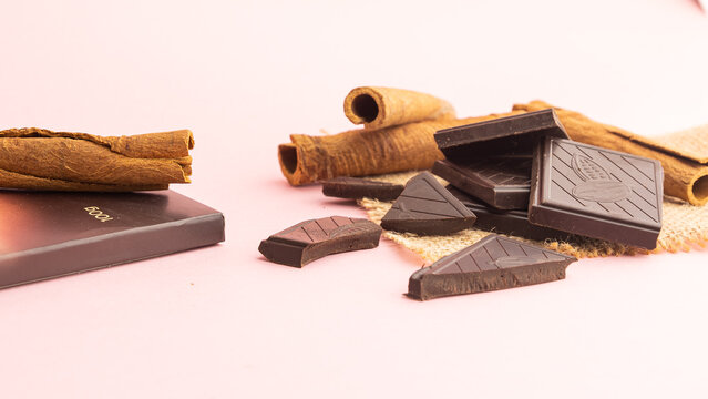 Trozos de chocolate negro minimalista y ramas de canela sobre un fondo rosa p&aacute;lido con espacio para texto