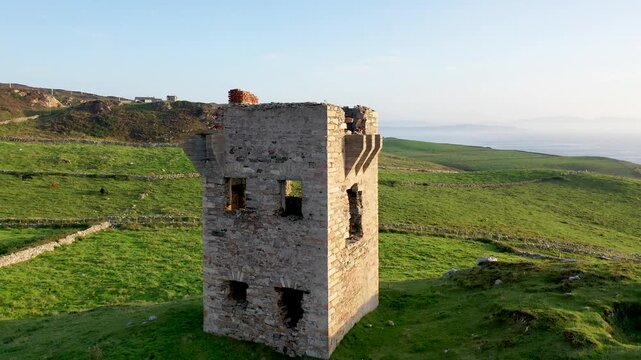 Aerial view of the historic stone signal tower at Crohy Head surrounded by lush green fields and rolling hills in Maghery, County Donegal, Ireland.