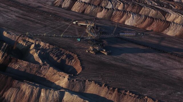 Aerial view of a massive bucket-wheel excavator operating in a deep open-pit coal mine with vast earth mounds and industrial excavation patterns in Leipzig, Saxony, Germany.