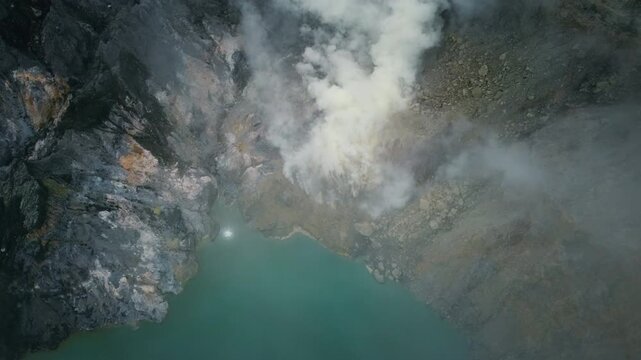 Thick white sulfur fumes rise from rocky vents along the edge of the turquoise Kawah Ijen crater lake in East Java, Indonesia.