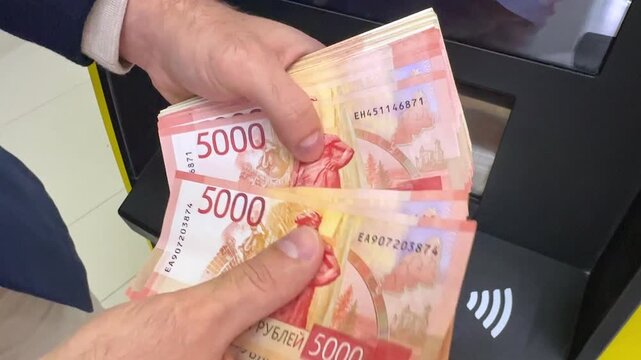 Close up man hands count a thick stack of Russian ruble banknotes, five thousand beside bank automated teller machine, showing red and pink currency details. Withdrawing cash from an ATM. footage