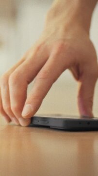 A man's hand reaches from the bed to the floor, searching for his phone to turn off the noisy alarm. Morning sunlight illuminates his arm as part of a daily lifestyle routine of waking up