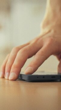 A man's hand hangs off the bed edge at home during morning hours, stretching fingers downward to locate and silence the device lying on the floor, theme of waking up and daily routine
