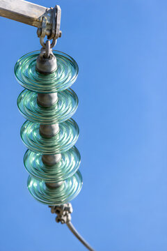 Close-up of a glass insulator string on a high voltage power line against a clear blue sky, with copy space