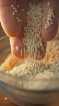 A man examines sesame grains in his cupped hands, letting them fall into a bowl during food manufacture, representing quality control processes in agriculture and agronomy