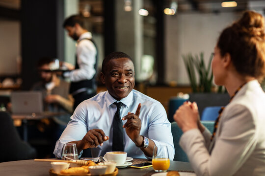 Smiling businessman gestures during breakfast meeting at cafe