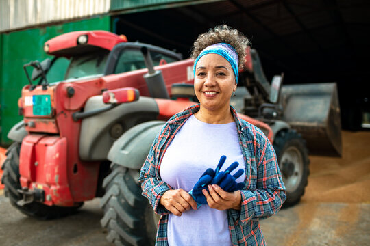 Smiling woman farmer holding gloves by tractor in barn