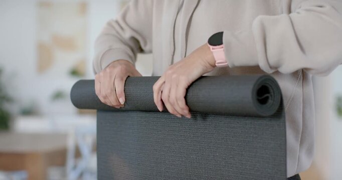 Gripping edge and shifting hands, woman is rolling dark gray mat in living area to store