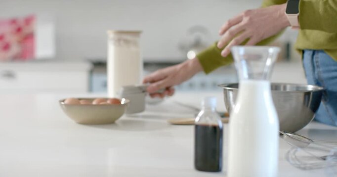 Hands are entering from right, centering eggs, lifting canister and arranging tools for baking prep