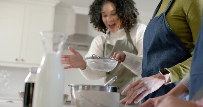 Diverse female cooks wearing aprons sifting stirring batter at home lifting sieve over bowl to bake