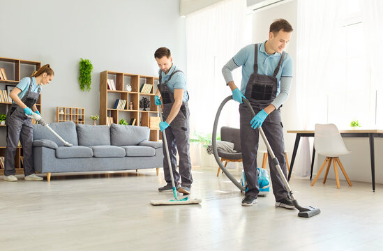 Cleaners team vacuuming and mopping housework service home. Crew in uniform with gloves cleans a bright living room, using vacuum and mop on hardwood flooring. Clean home hygiene team concept.