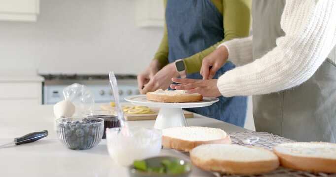 Positioning layer on rotating stand, two bakers are steadying, spreading frosting and stacking cake