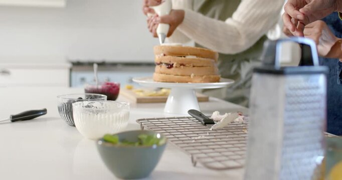 African American women in green blue aprons icing cake with piping bag, hands rising above kitchen
