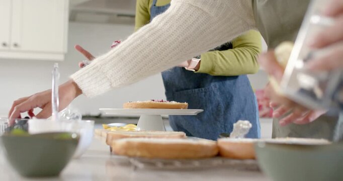 Jar being passed, aproned is scooping jam onto cake stand, partner is passing tools for stacking