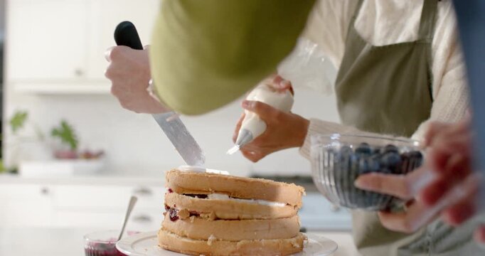 Placing cake on rotating stand, two cooks are filling, smoothing, piping blueberries to finish cake