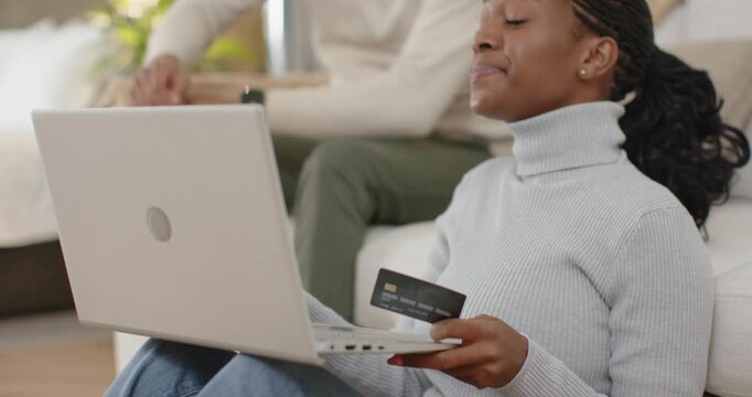 Diverse couple sitting on living room floor entering card info on white laptop, confirming purchase