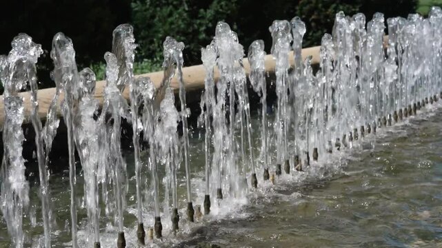 Close-up video of multiple fountain jets shooting clear water in bright sunlight, creating sparkling droplets and rhythmic flowing patterns. The refreshing water display is ideal for summer, cooling