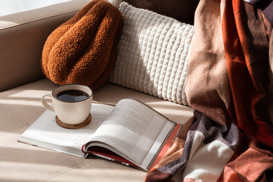 Cozy scene with coffee and book on sofa warm blanket and textured pillows