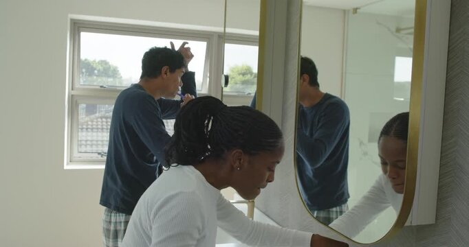 Couple brushing teeth with yellow, blue brushes at sink preparing for day, rinsing, man fixing hair