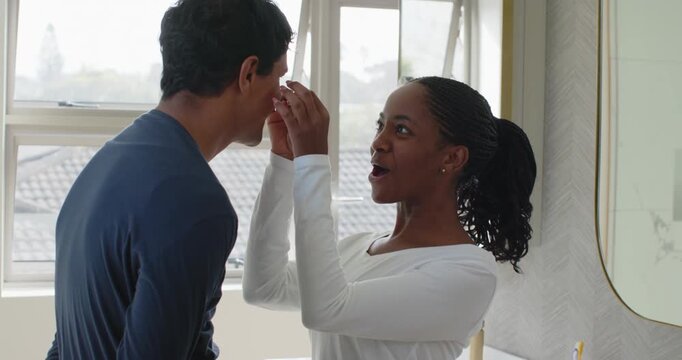 Couple at vanity mirror, woman in pjs opening packet applying undereye cream for care then smiling