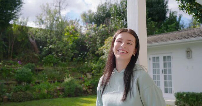 Woman in 20s on porch wearing mint hoodie by white post spotting camera turning smiling laughing