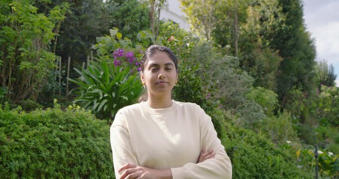 Indian woman arms crossed, smiling and laughing as camera moving closer in yard near purple flowers