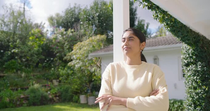 Indian woman shifting gaze by post on covered patio in cream top, sun breaking, smiling laughing