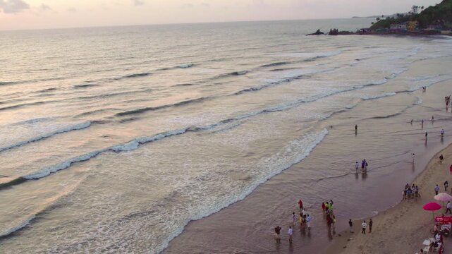 Aerial view of Mandrem Beach at sunset with gentle waves and people walking along the shoreline in Mandrem, Goa, India.
