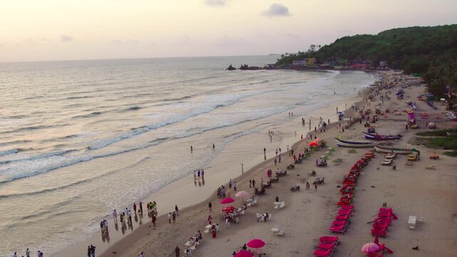 Aerial view of Mandrem Beach with waves, sand, beach umbrellas, and people in Mandrem, Goa, India.