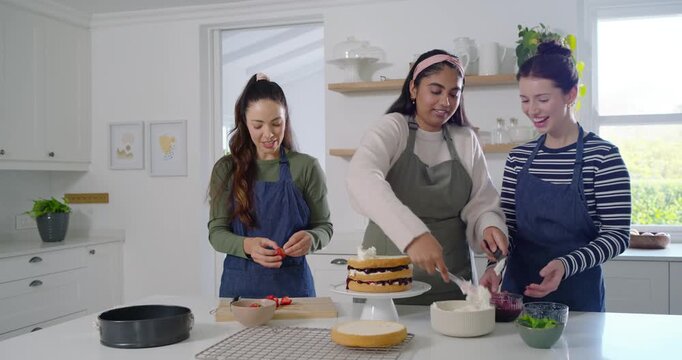 Diverse women collaborating on cake assembly at kitchen island, center placing layers on cake stand
