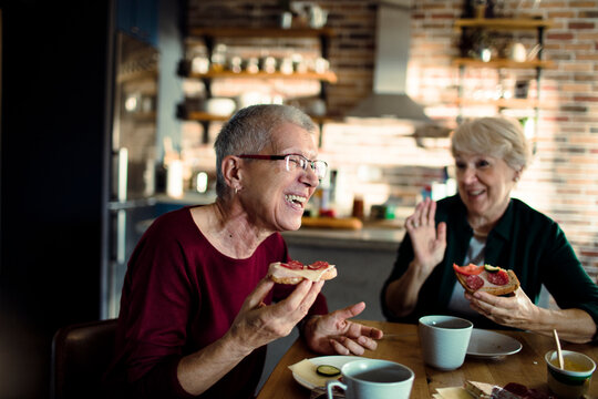 Two senior women laughing and eating sandwiches at home